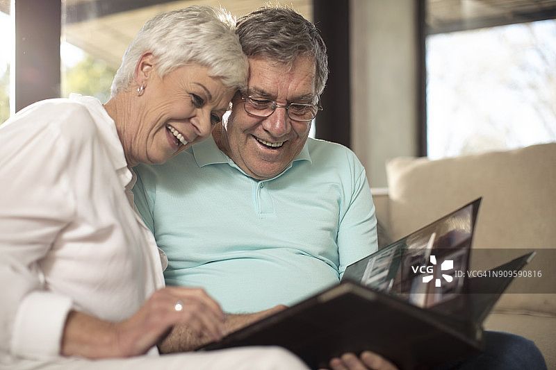 一对快乐的老夫妇坐在沙发上看相册图片素材