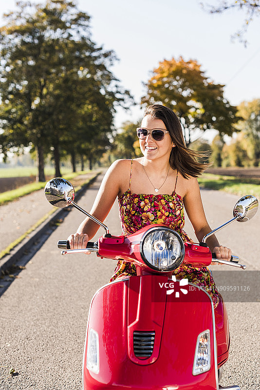 快乐的年轻女子骑摩托车在乡村公路上图片素材