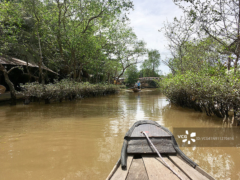 越南湄公河三角洲运河上，长桨划艇正靠近木船船头图片素材