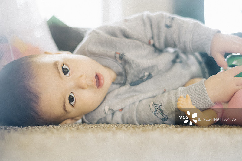 18个月大的黑发小孩抱着一个娃娃，躺在家里的地毯上图片素材