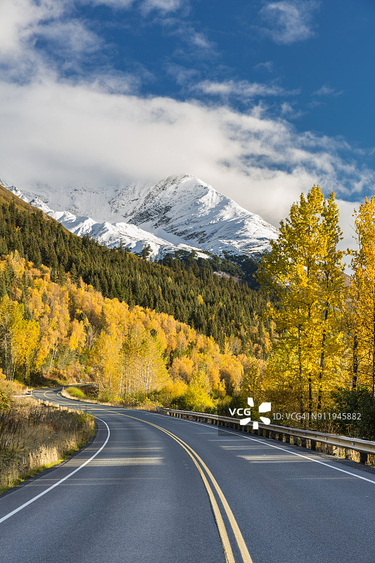 白雪皑皑的基奈山脉使苏厄德公路显得矮小，黄叶覆盖的树木在秋天的道路上排列，阿拉斯加中南部图片素材