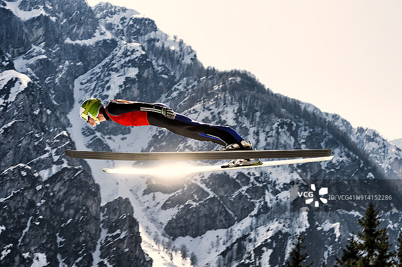 侧视图的年轻男子滑雪跳台在半空中，太阳反射图片素材