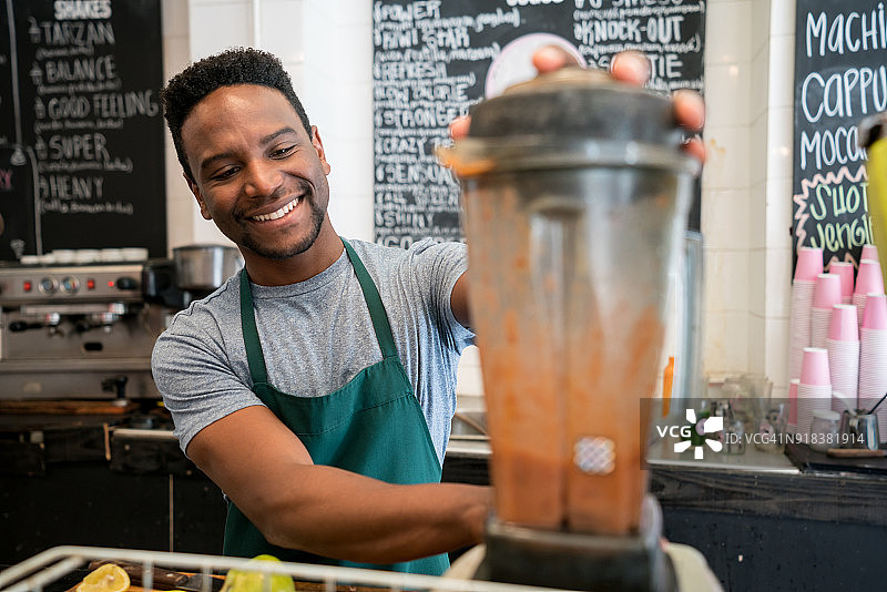 一个黑人推销员在果汁机里做果汁，看起来很开心，而且面带微笑图片素材