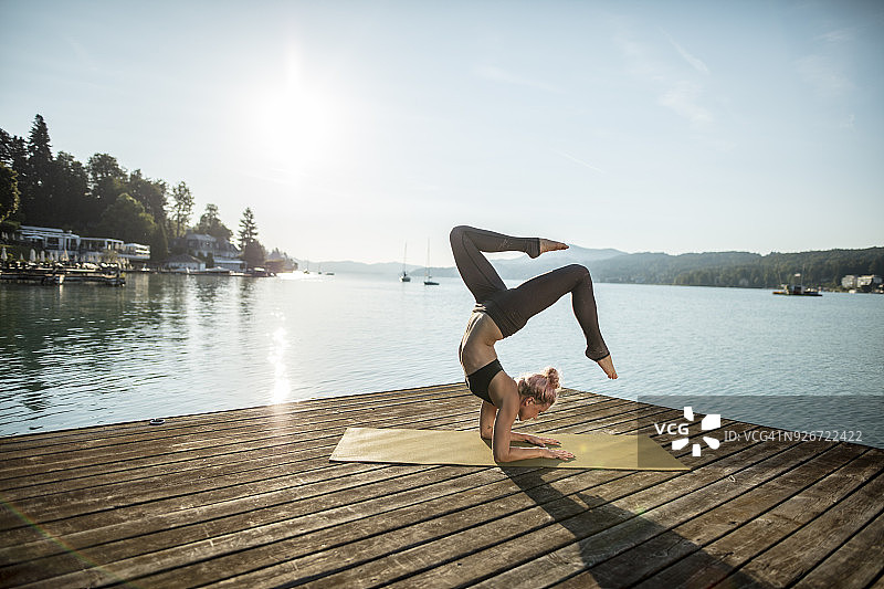 一个女人在湖边的码头上练习瑜伽图片素材