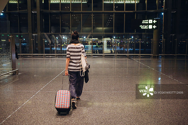 带着行李箱独自在卡塔尔机场旅行的年轻女子图片素材