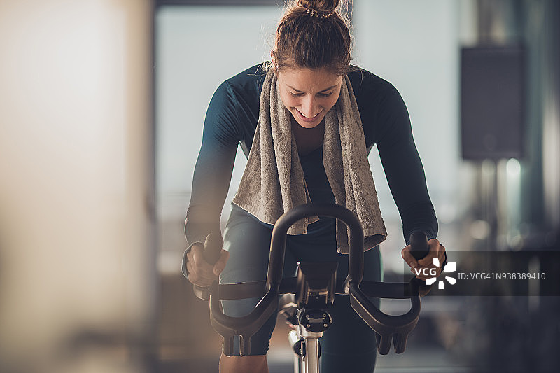 快乐的运动女人在健身房骑自行车锻炼。图片素材