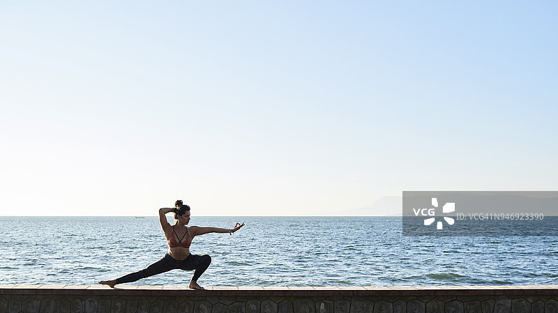 一个年轻女子在海边的一堵墙上练习瑜伽图片素材
