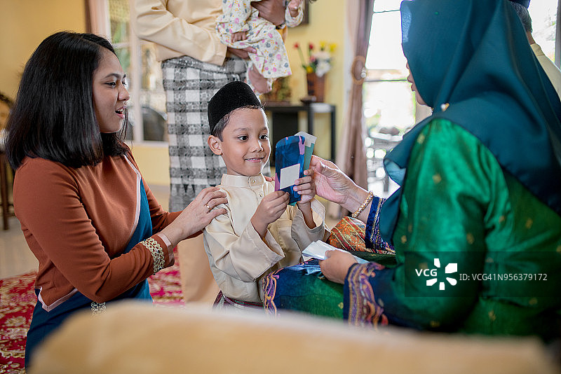 作为伊斯兰教开斋节庆祝活动的一部分，小男孩从他的祖父母那里得到了一份礼物。图片素材