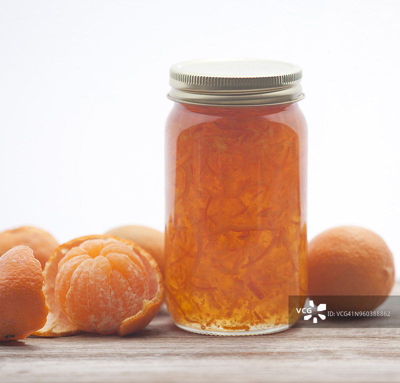 装橘子果酱的罐子，周围是去皮的整个橘子，放在旧的木头表面上图片素材