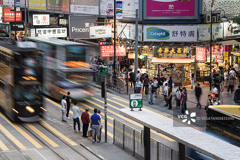 在香港著名的购物区铜锣湾，一辆巴士和一辆有轨电车在街道上奔跑图片素材