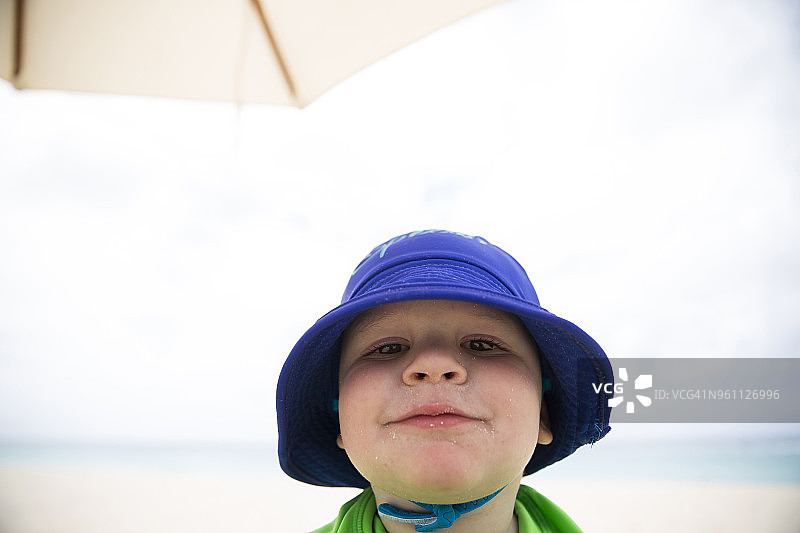 男孩戴着帽子站在海滩上，对着天空的特写图片素材
