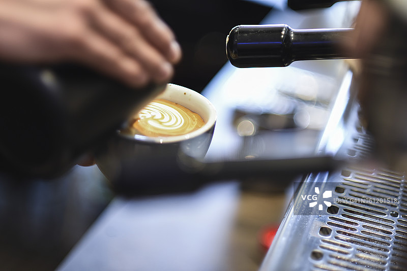 在咖啡馆里，咖啡师在制作泡沫饮料时将牛奶倒进咖啡里图片素材