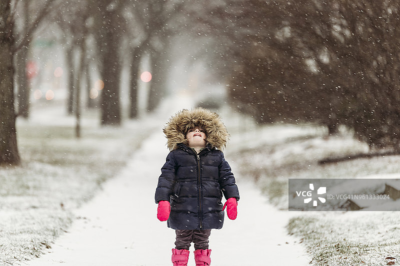 在下雪的时候，穿着带帽夹克的女孩在雪道上用舌头捕捉雪花图片素材