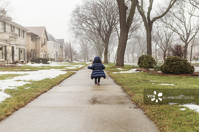 后视图的女孩穿着兜帽夹克，而在人行道上跑步在冬天图片素材