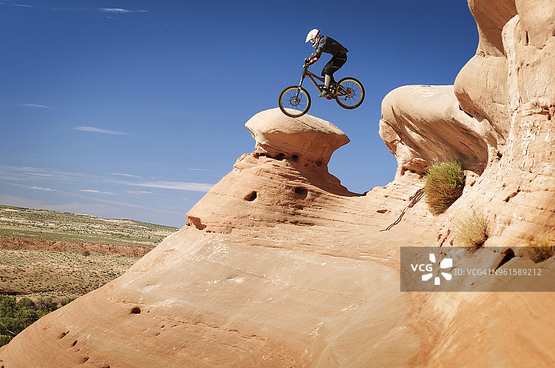 骑自行车的人在蓝天下从山上跳下来的侧视图图片素材