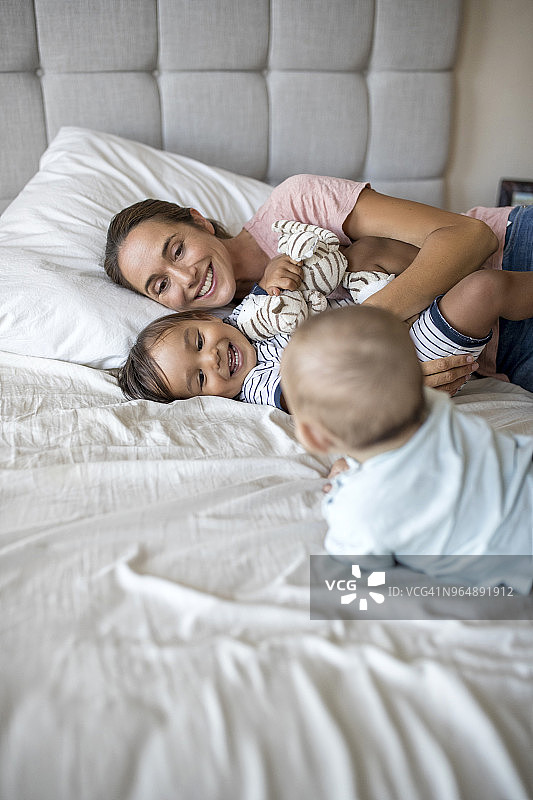 抱着婴儿和蹒跚学步的婴儿躺在床上的妇女图片素材