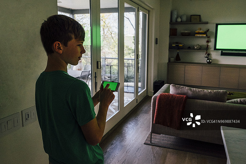 十几岁的男孩拿着智能手机和绿色屏幕电视在背景图片素材