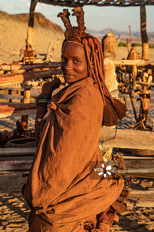 在纳米比亚Sesfontein附近的Puros村，身着传统服饰的赭红色的辛巴族妇女在傍晚的灯光下害羞地微笑着(模特释放)图片素材