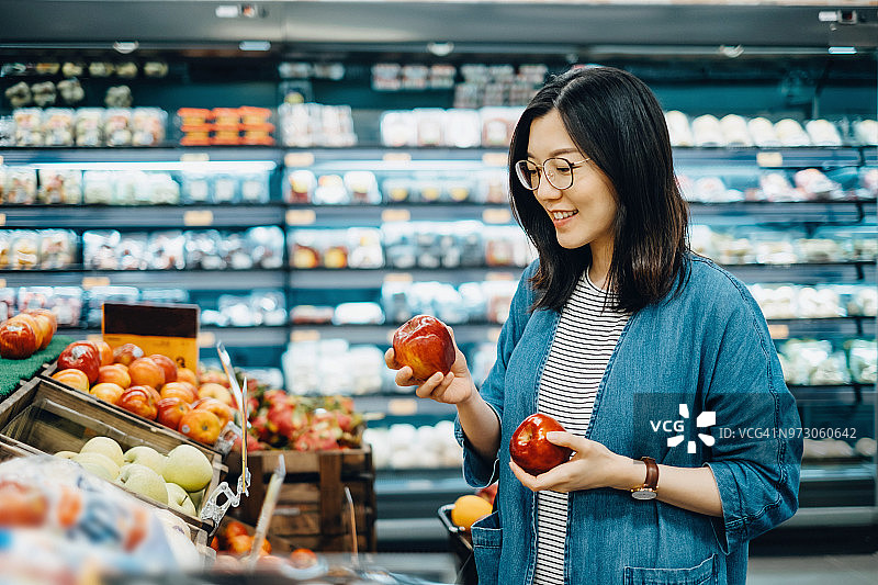 年轻的亚洲妇女在超市购买新鲜的有机水果图片素材