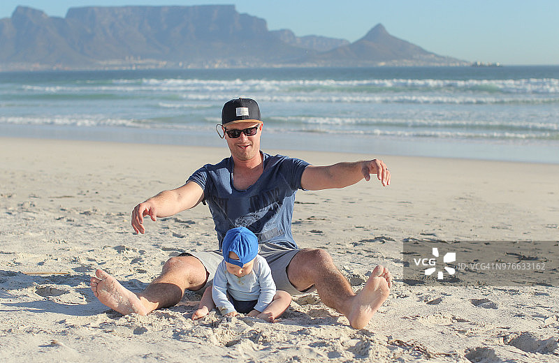 一位年轻的父亲和他的小儿子在海滩上玩耍。图片素材