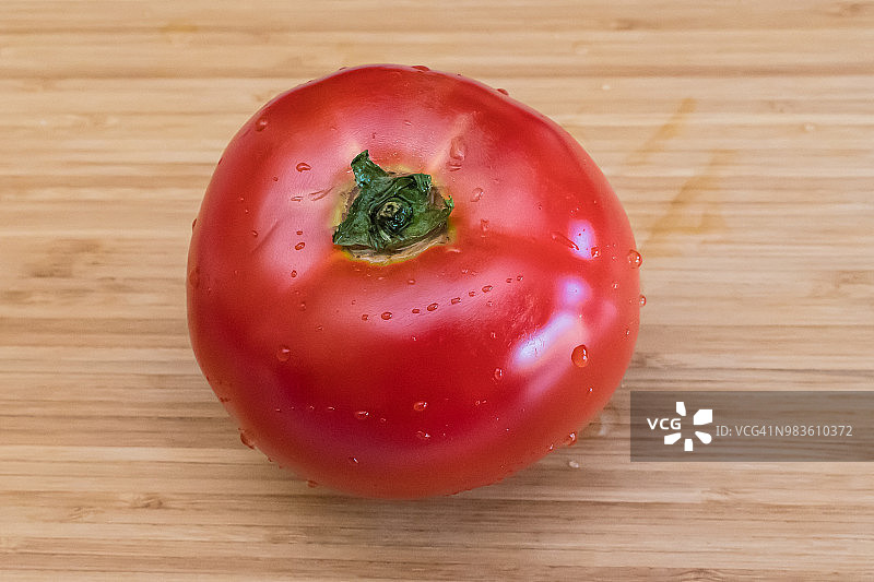一个湿的红番茄在木砧板上的特写图片素材
