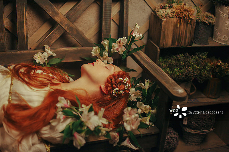 美丽的红头发女孩躺在花丛中图片素材