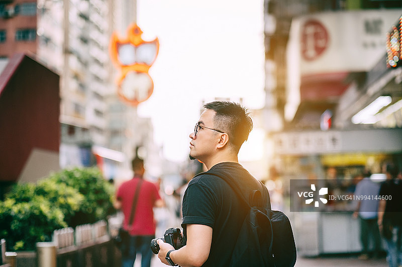 年轻的男游客带着相机在香港旅行，探索当地的城市街道图片素材