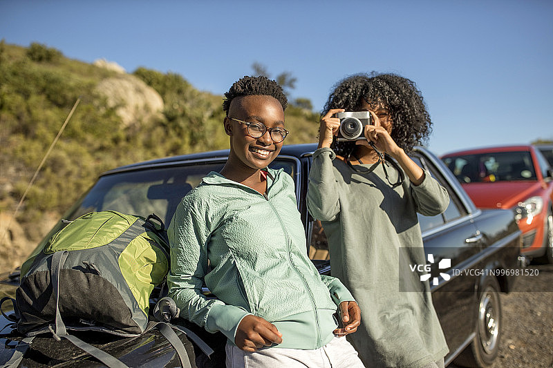 两个背着背包的年轻女子靠在一辆车上拍照图片素材