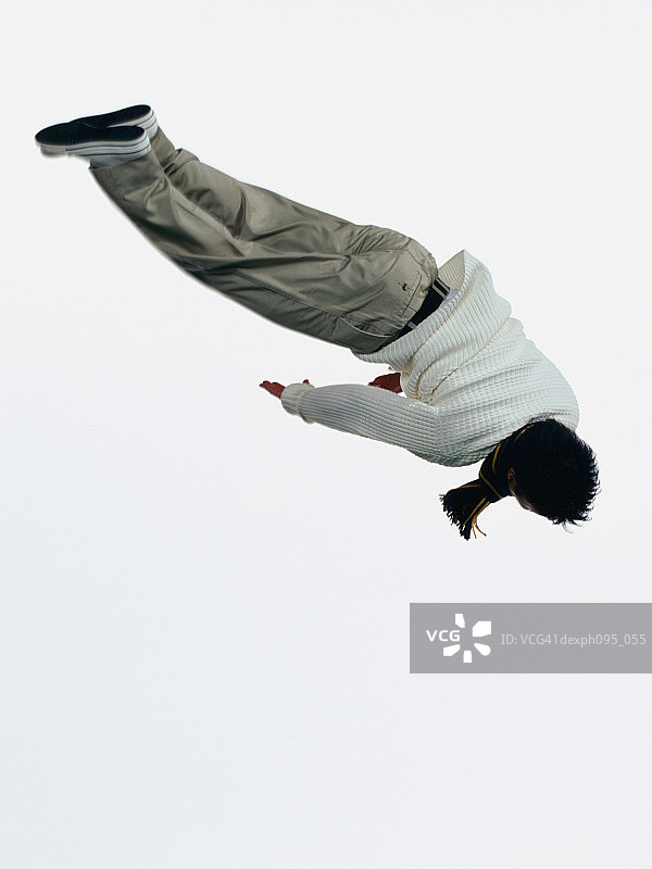 年轻的亚洲男子在裤子和运动衫和围巾，跳在半空中图片素材