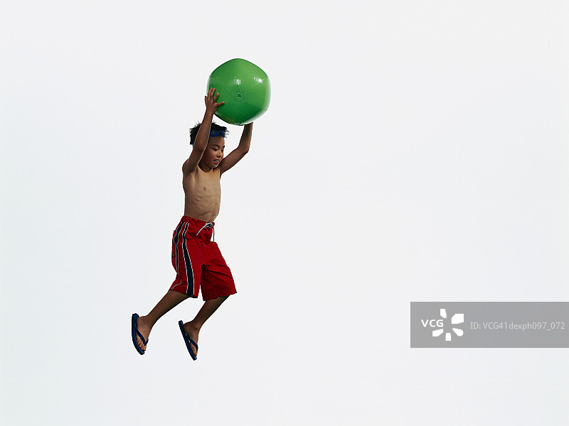 年轻的亚洲男孩拿着沙滩球，在半空中跳跃图片素材