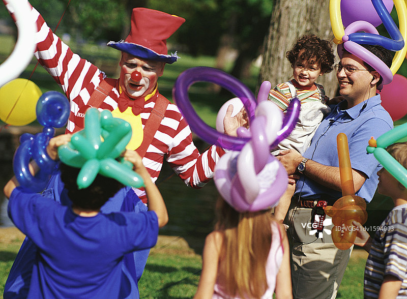 在一个生日聚会上，小丑在一群孩子和一位父亲面前用气球表演图片素材