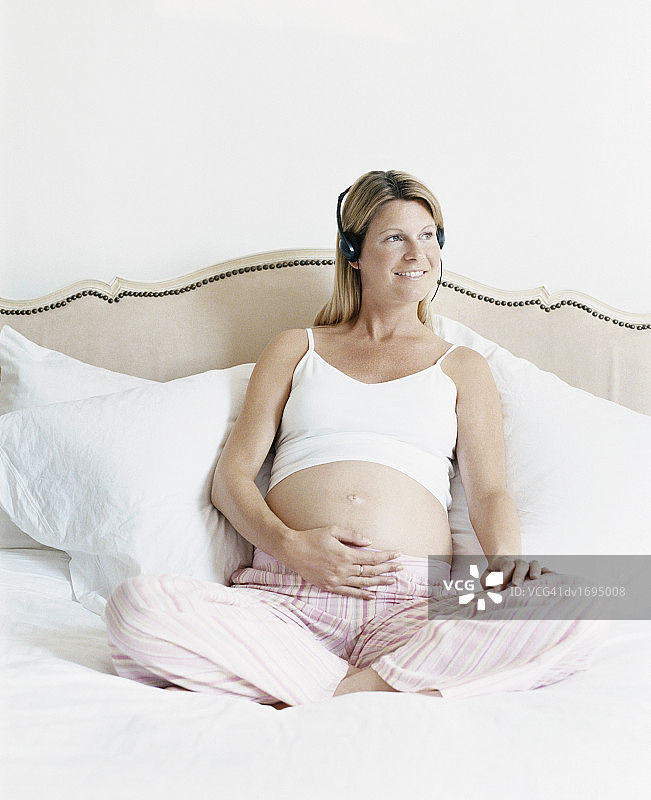 孕妇坐在床上听耳机图片素材