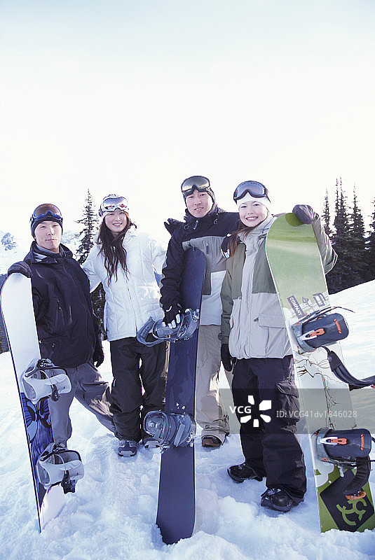 四名穿着滑雪服的青年男子和女子手持滑雪板站在滑雪斜坡上图片素材