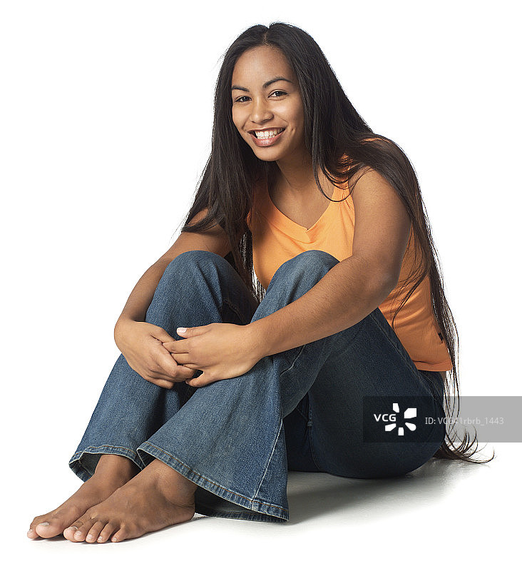 一个穿着牛仔裤和橙色衬衫的少数民族少女坐下来，笑容灿烂图片素材