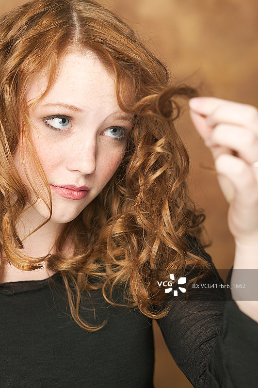 一个穿着黑色衬衫的红发少女的肖像，她在检查她的卷发末端图片素材
