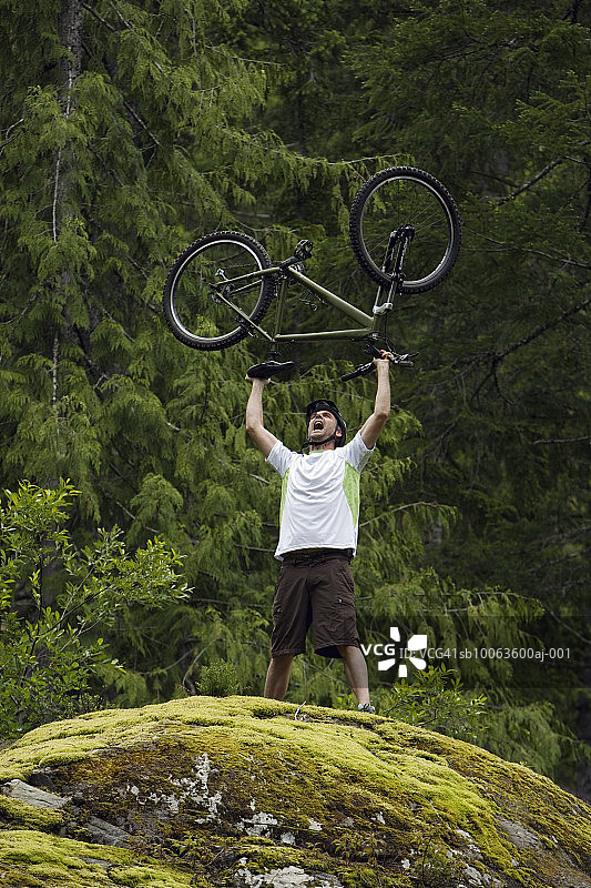 一个成熟的男人把自行车举过头顶站在巨石上图片素材