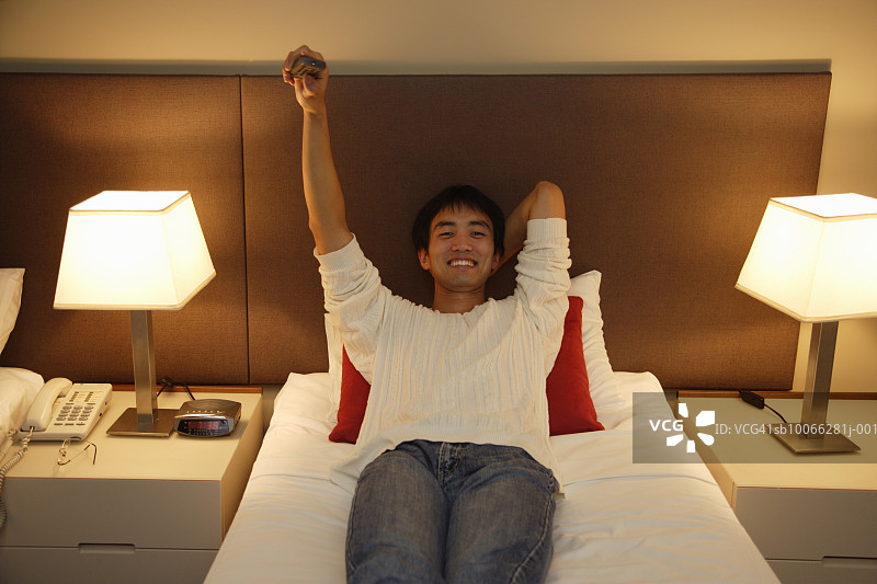 一个年轻人躺在旅馆房间的床上看电视图片素材