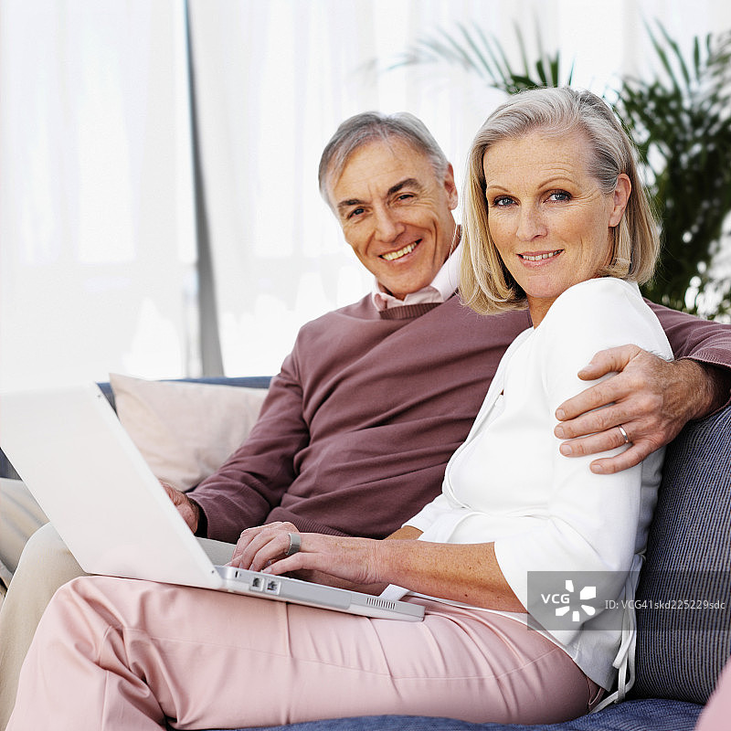 一对成熟的夫妇坐在沙发上用笔记本电脑工作的特写图片素材
