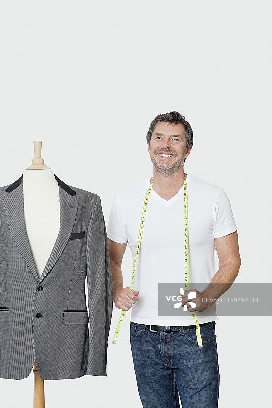 在灰色背景下，成熟的男性裁缝站在裁缝的假人旁边图片素材
