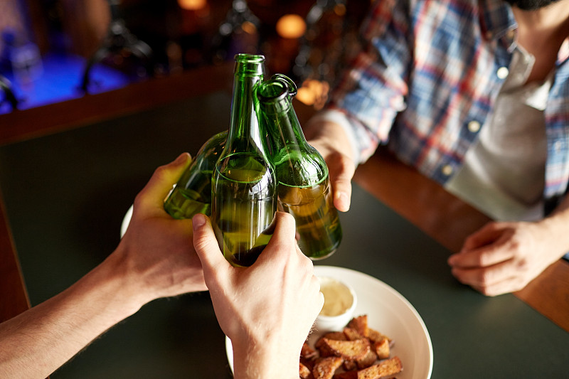 人们，男人，休闲，友谊和庆祝概念-近距离男性朋友喝啤酒和在酒吧或酒吧碰杯图片素材
