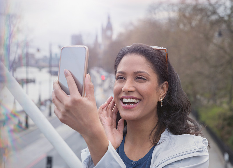 微笑，自信的女人在城市的桥上用手机自拍图片下载
