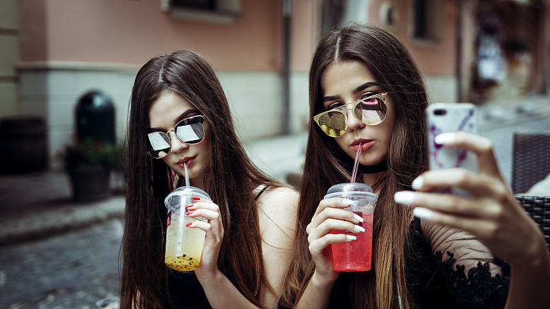 两个年轻的女人戴着太阳镜在城市街道上自拍图片下载