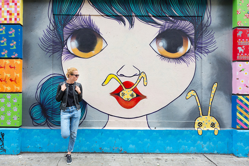 美国纽约，一名女子靠在彩色涂鸦墙上讲着智能手机。图片下载