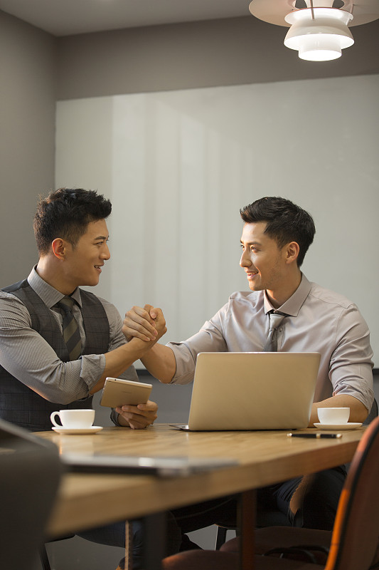 商务青年男子使用笔记本电脑在公司会议室讨论工作握手庆祝达成共识图片下载