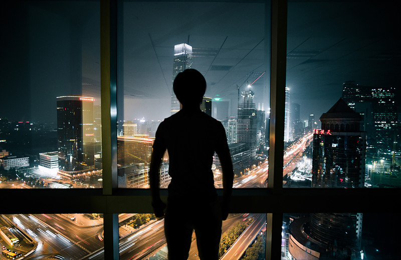 成年男性在办公室内透过窗户看城市CBD夜景图片下载
