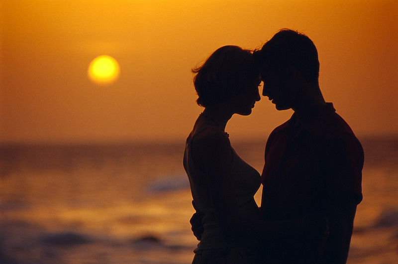 海滩上的日落映出男人和女人的剪影图片下载