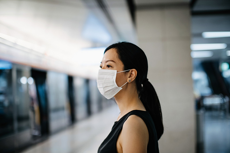 一名亚洲妇女戴着防护口罩在月台等候地铁列车图片下载