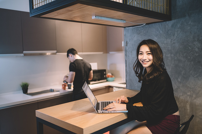 亚洲华人夫妇在厨房准备咖啡和使用笔记本电脑图片下载