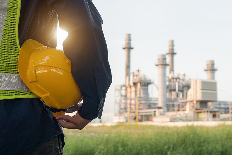 一名戴着白色安全帽的工程人员站在重石化工业炼油厂建筑结构前图片下载