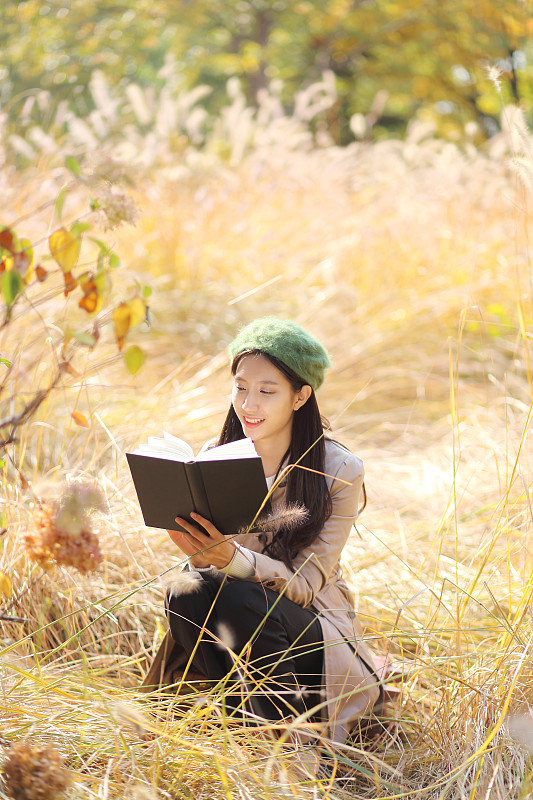 年轻女子在秋天的公园里看书图片下载